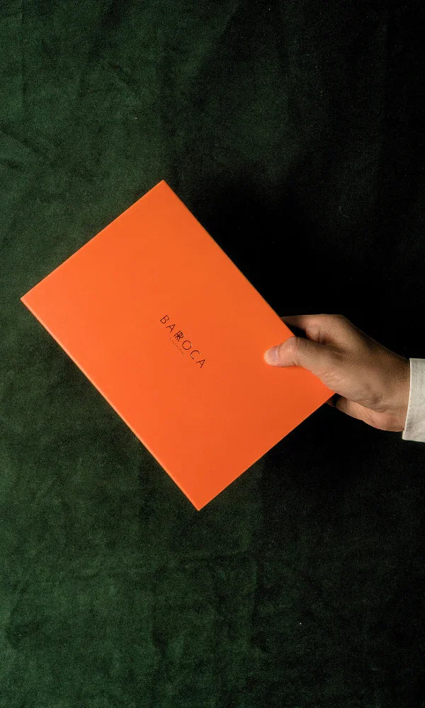 Caja naranja de Barroca Chocolates sostenida sobre fondo verde oscuro